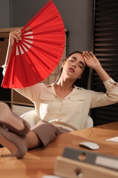 Woman with hand fan suffering from heat at home. Summer season