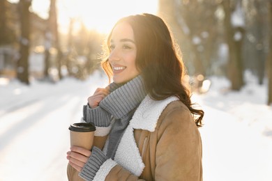 Photo of Portrait of smiling woman with paper cup of coffee in snowy park