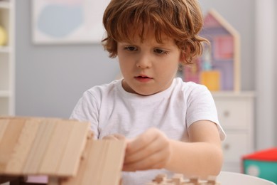 Photo of Little boy playing with wooden construction set in room, closeup. Child's toy