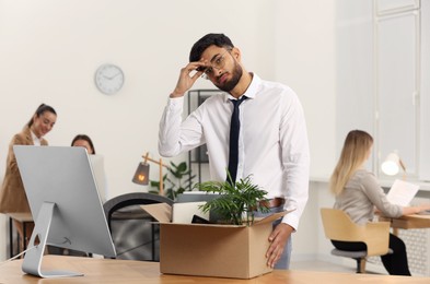 Photo of Unemployment problem. Frustrated man with box of personal belongings at table in office