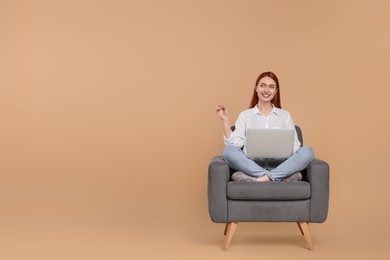 Photo of Smiling young woman with laptop sitting in armchair against beige background, space for text