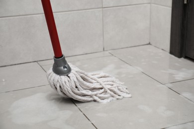 Photo of Cleaning grey tiled floor with string mop, space for text