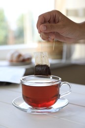Photo of Woman taking tea bag outcup at white wooden table indoors, closeup