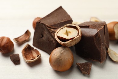 Photo of Delicious chocolate chunks and hazelnuts on white table, closeup