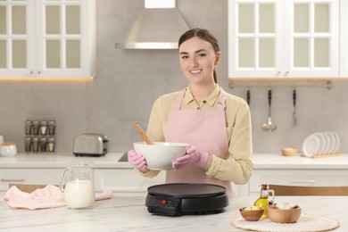Photo of Young woman cooking delicious crepes in kitchen