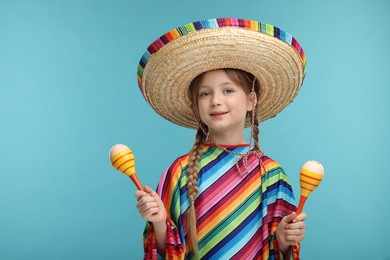 Cute girl in Mexican sombrero hat and poncho with maracas on light blue background