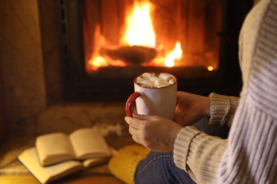 Photo of Woman with cup of hot cocoa near fireplace at home, closeup. Space for text