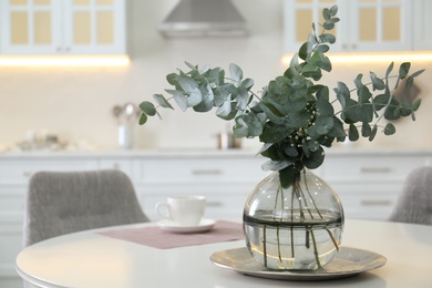 Beautiful eucalyptus branches on white table in kitchen, space for text. Interior element