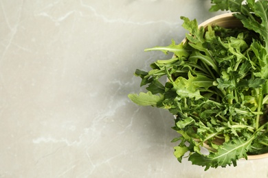Photo of Fresh arugula in bowl on light grey marble table, top view. Space for text