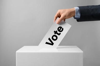Photo of Man putting his vote into ballot box on light background, closeup