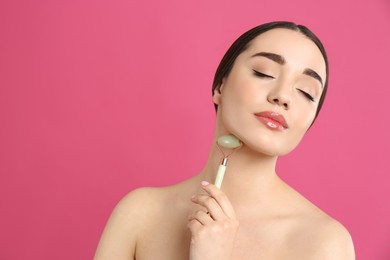 Photo of Woman using natural jade face roller on pink background, space for text