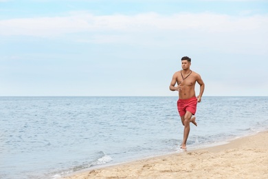 Photo of Handsome male lifeguard running on sandy beach