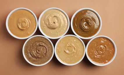 Photo of Many tasty nut butters in bowls on beige table, flat lay