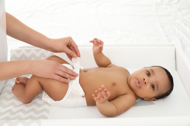 Mother changing her baby's diaper on table indoors