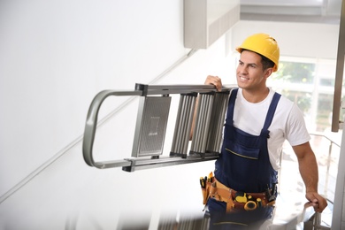 Photo of Professional builder carrying metal ladder up stairs