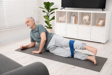 Photo of Senior man doing exercise with fitness elastic band on mat at home