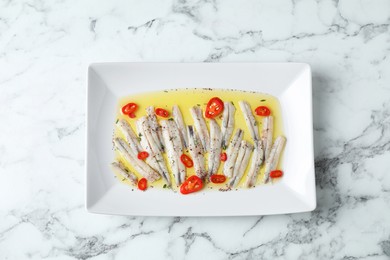 Photo of Tasty pickled anchovies with spices on white marble table, top view