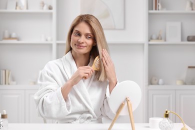 Beautiful woman brushing her hair at white table in room