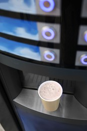 Photo of Coffee and hot beverage vending machine with paper cup on drip tray, above view