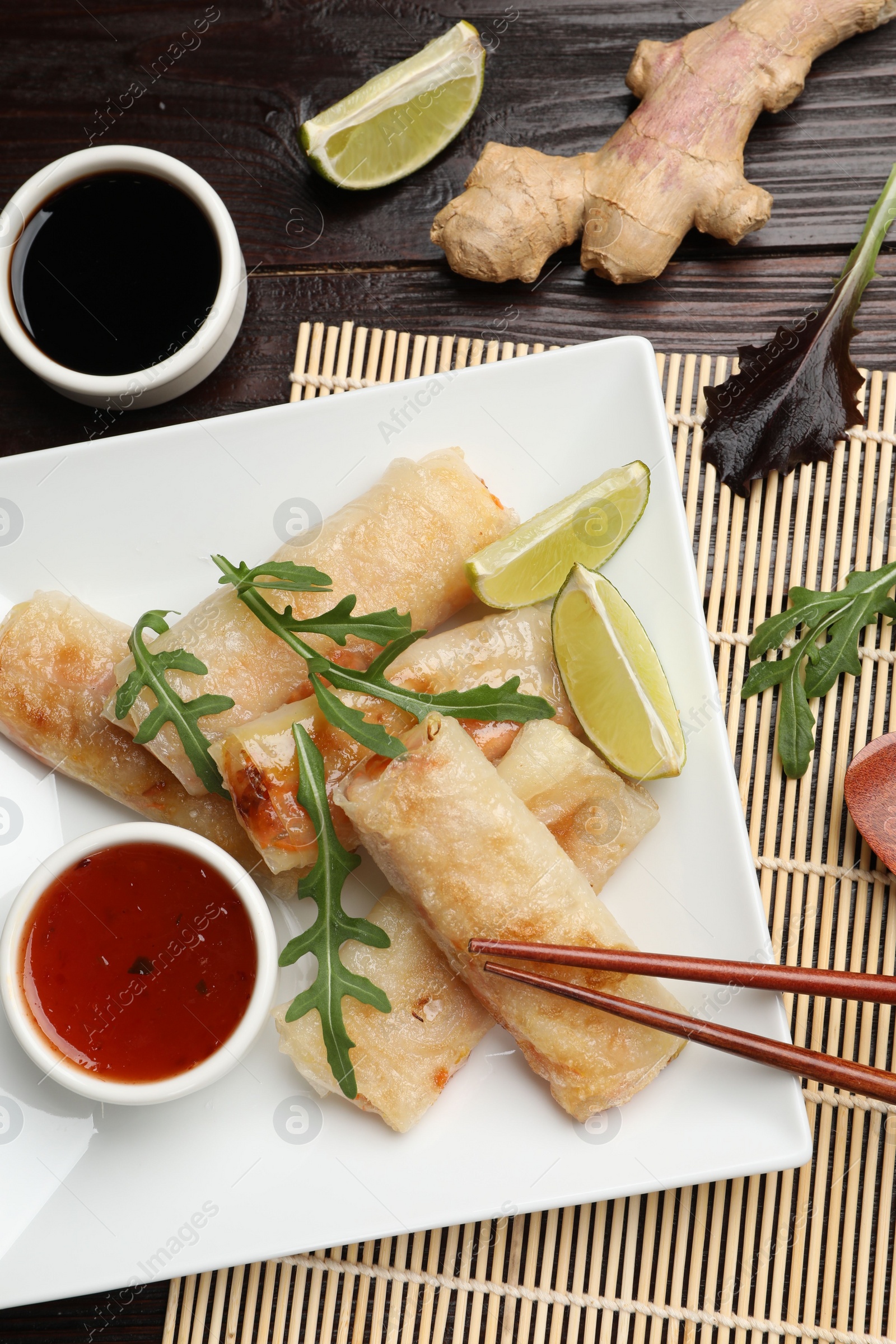 Tasty fried spring rolls, arugula, lime and sauces served on wooden table, flat lay Photo of Tasty fried spring rolls, arugula, lime and sauces served on wooden table, flat lay