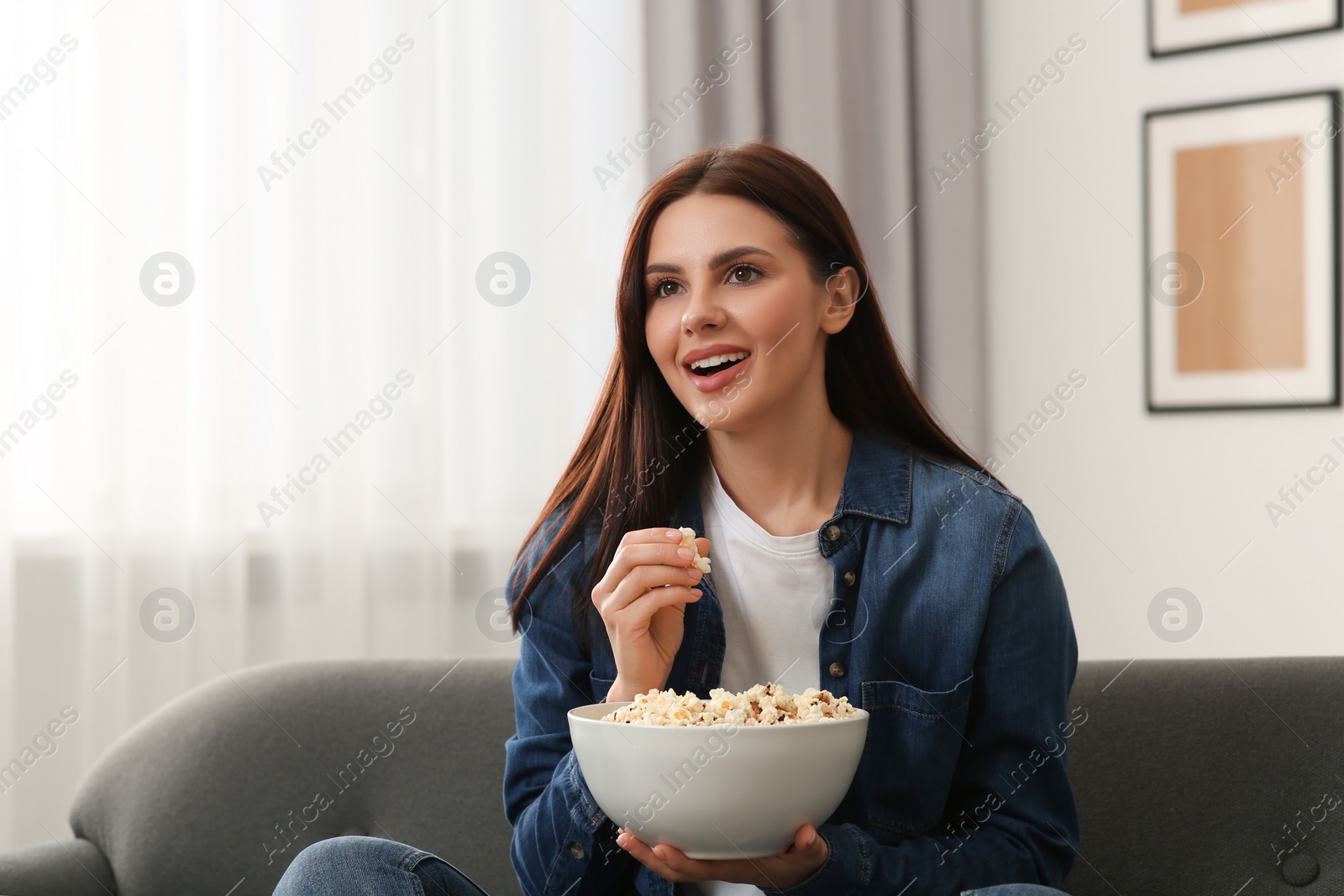 Photo of Beautiful woman with bowl of popcorn watching TV at home