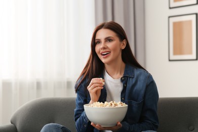 Photo of Beautiful woman with bowl of popcorn watching TV at home