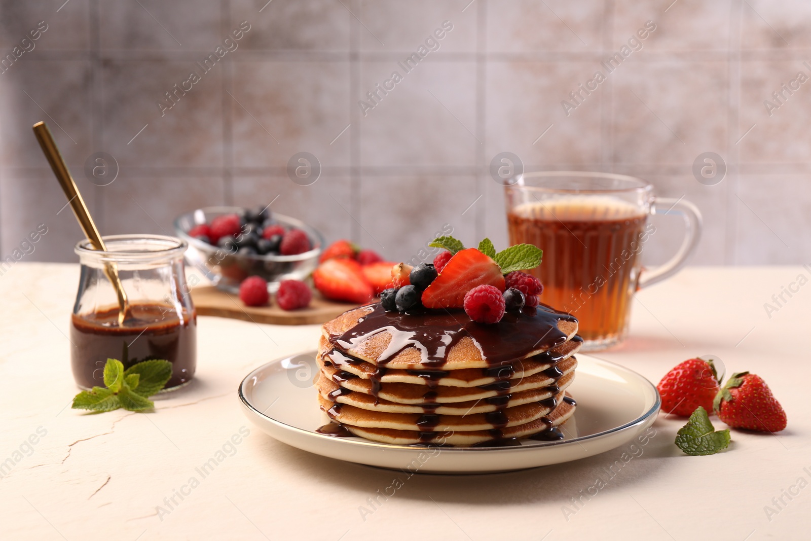 Photo of Stack of tasty pancakes with fresh berries, chocolate sauce and mint on white table