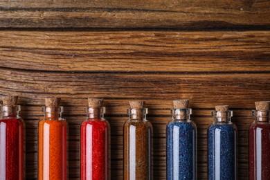 Photo of Glass bottles with different food coloring on wooden table, flat lay. Space for text