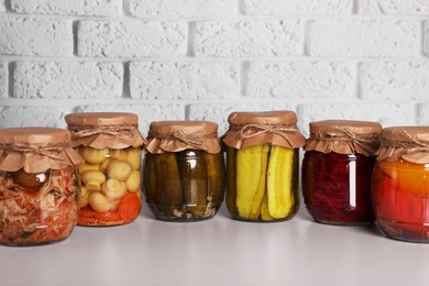 Photo of Many glass jars with different preserved vegetables and mushrooms on light grey table