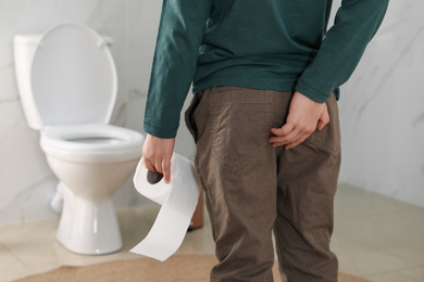 Photo of Boy with toilet paper suffering from hemorrhoid in rest room, closeup