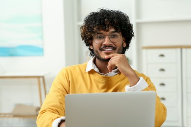 Photo of Handsome smiling man using laptop in room