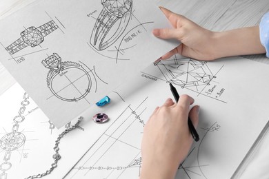 Photo of Jeweler with sketches of elegant jewelry at white wooden table, closeup