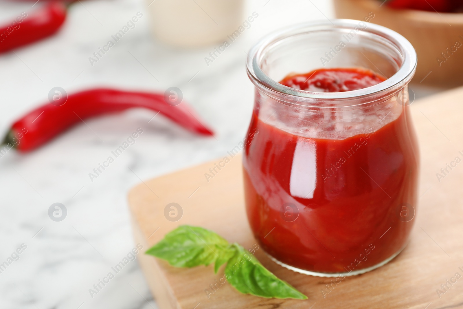 Photo of Jar with spicy chili sauce on marble table