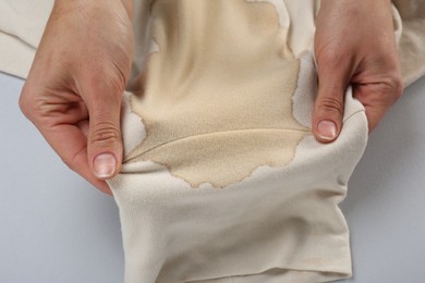 Photo of Woman holding beige sweater with stain on light grey background, closeup