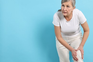 Photo of Arthritis symptoms. Woman suffering from pain in knee on light blue background, space for text