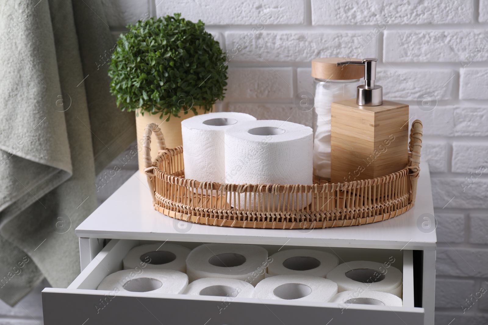 Toilet paper rolls, floral decor, dispenser and cotton pads on chest of drawers indoors Photo of Toilet paper rolls, floral decor, dispenser and cotton pads on chest of drawers indoors