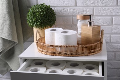 Photo of Toilet paper rolls, floral decor, dispenser and cotton pads on chest of drawers indoors