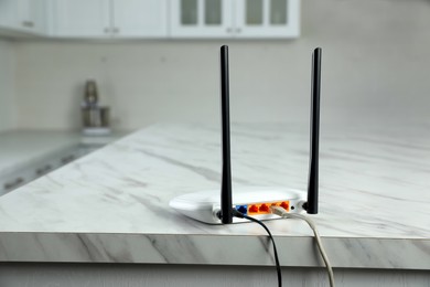 Photo of Modern Wi-Fi router on white marble table in kitchen
