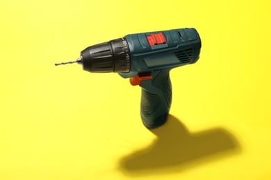 Photo of Modern electric power drill on yellow background