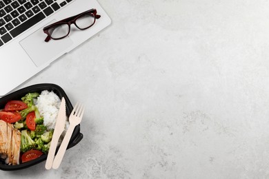Photo of Container of tasty food, laptop, cutlery and glasses on light grey table, flat lay with space for text. Business lunch