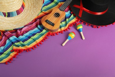 Photo of Composition with Mexican sombrero and black Flamenco hats, ukulele and maracas on purple table, above view. Space for text