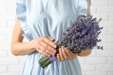 Woman holding fresh lavender flowers against white brick wall, closeup view