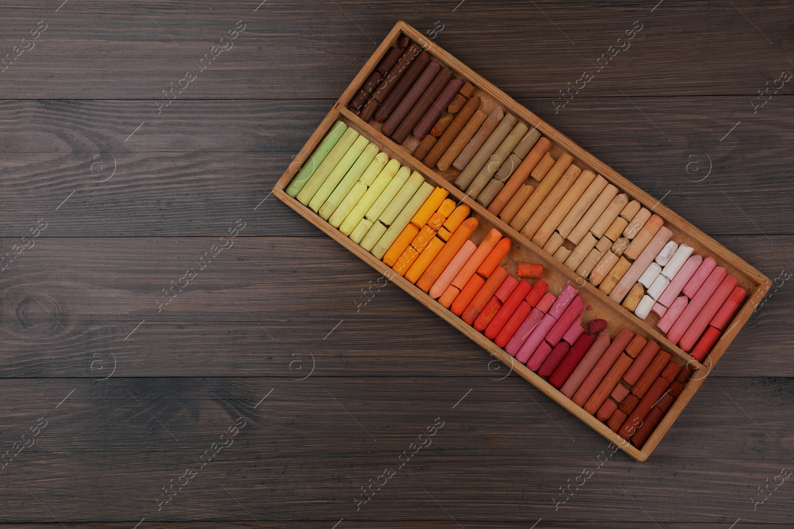 Photo of Drawing pastel set in box on wooden background, top view. Space for text