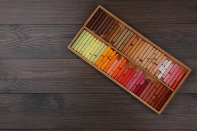 Photo of Drawing pastel set in box on wooden background, top view. Space for text