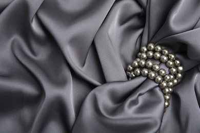 Photo of Beautiful pearls with grey silk as background, top view. Space for text