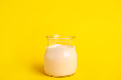 Photo of Tasty organic yogurt in glass jar on yellow background