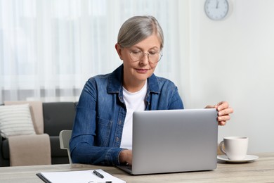 Photo of Beautiful senior woman using laptop at wooden table indoors