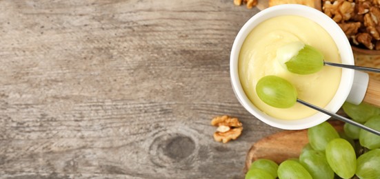 Image of Dipping grapes into fondue pot with white chocolate on wooden table, top view with space for text. Banner design