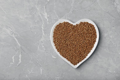 Heart shaped plate with raw buckwheat on grey background, top view. Space for text