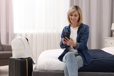Photo of Smiling guest with smartphone relaxing on bed in stylish hotel room
